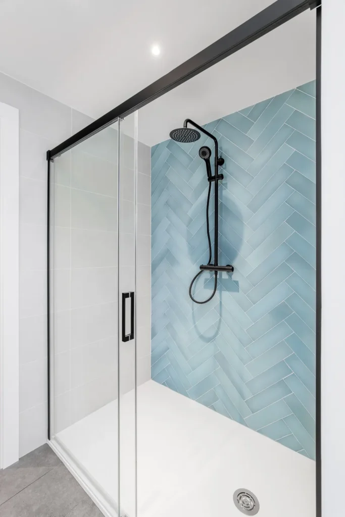 Glass shower door with a black frame and blue tile wall
