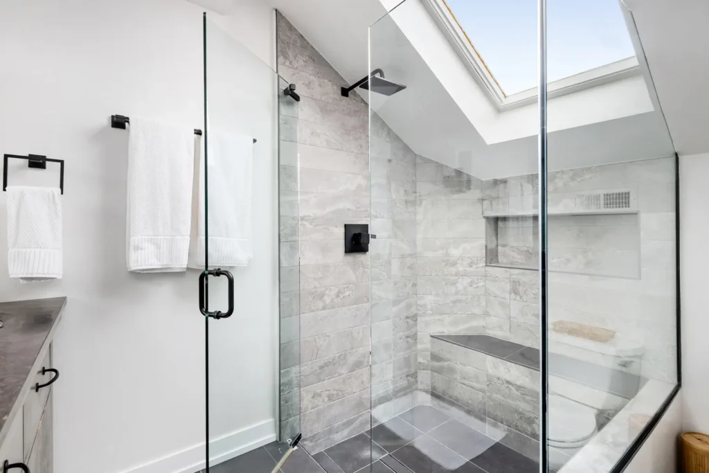 Frameless glass shower door with black hardware under a skylight
