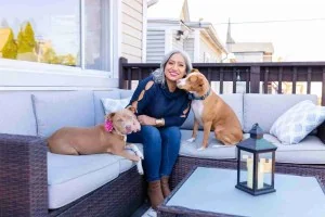 Carla Casas seated outdoors with two dogs in her official biography photo