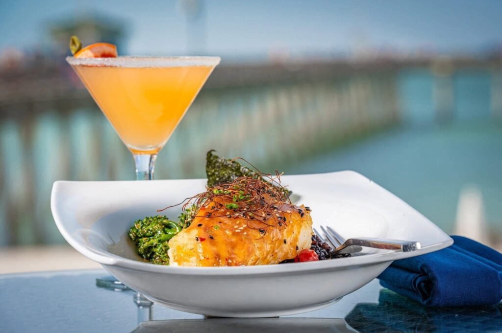 Fish entree and orange cocktail with the pier in the background; Fins at Sharky's gallery