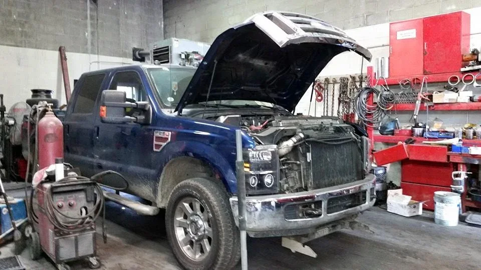 Blue pickup truck with its hood open inside a repair workshop